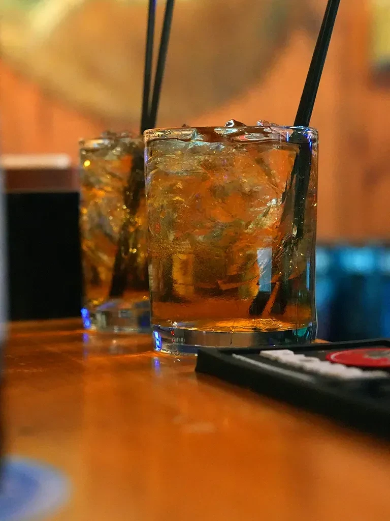 Two golden-brown iced drinks with straws on a bar.