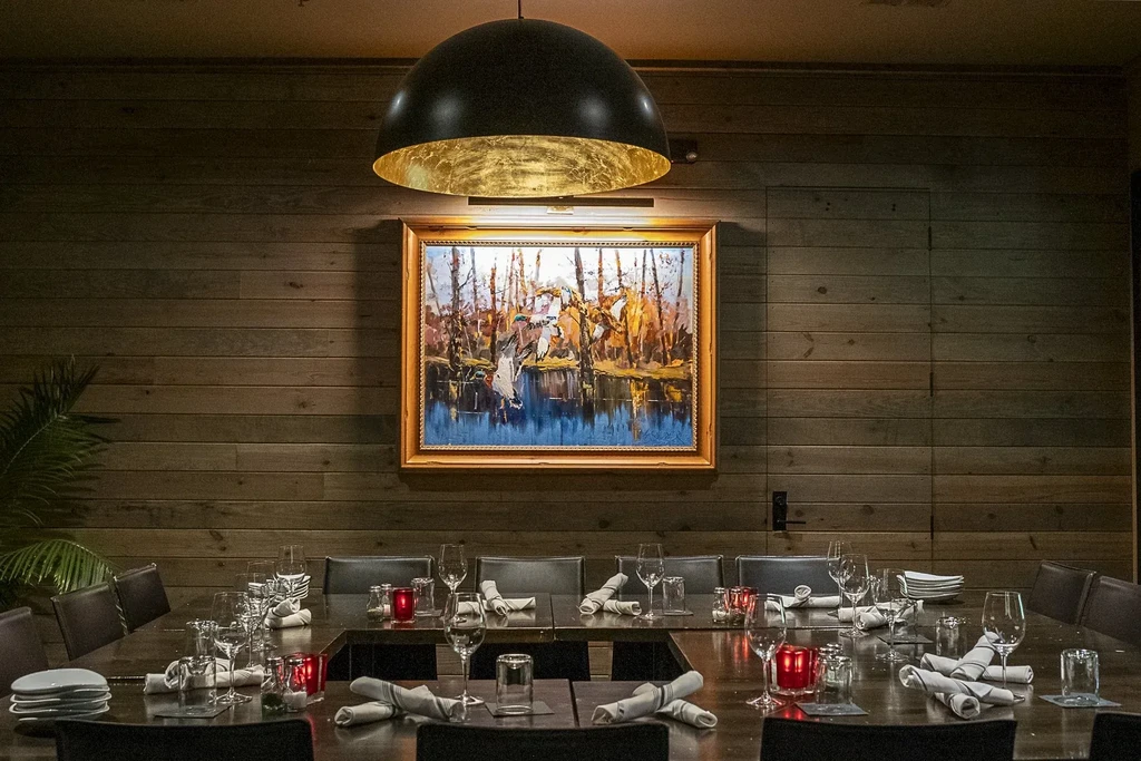 Private dining room with U-shaped table, gold pendant, autumn landscape painting.