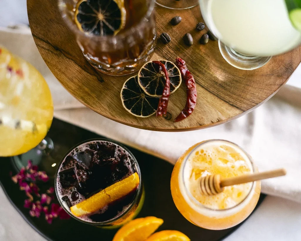 Overhead view of colorful drinks with garnishes on a tray and dark surface.