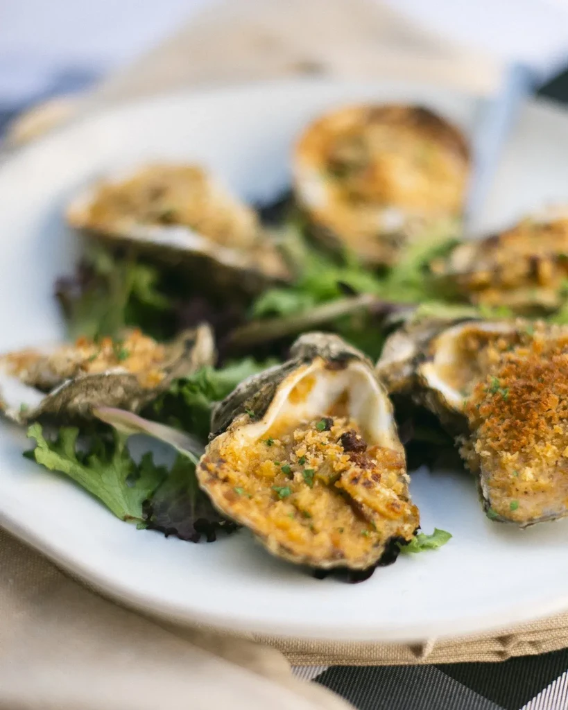 Several baked oysters with golden-brown crumb topping on lettuce.