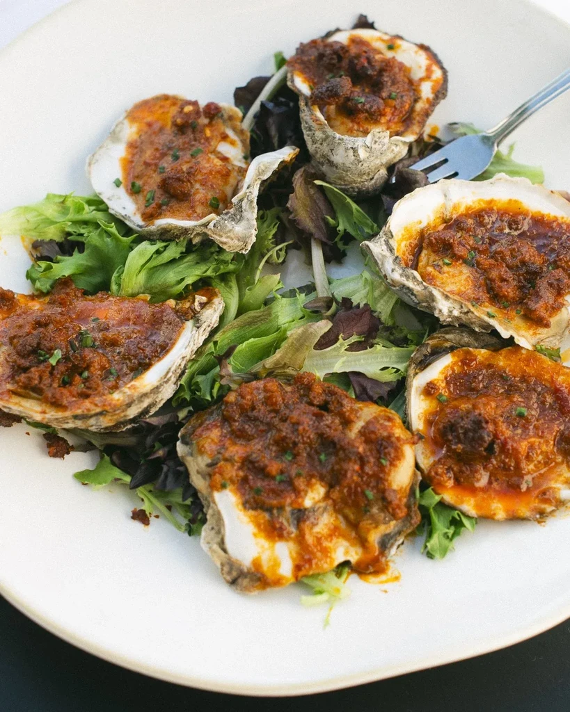 Six oysters on the half shell with savory topping and greens.