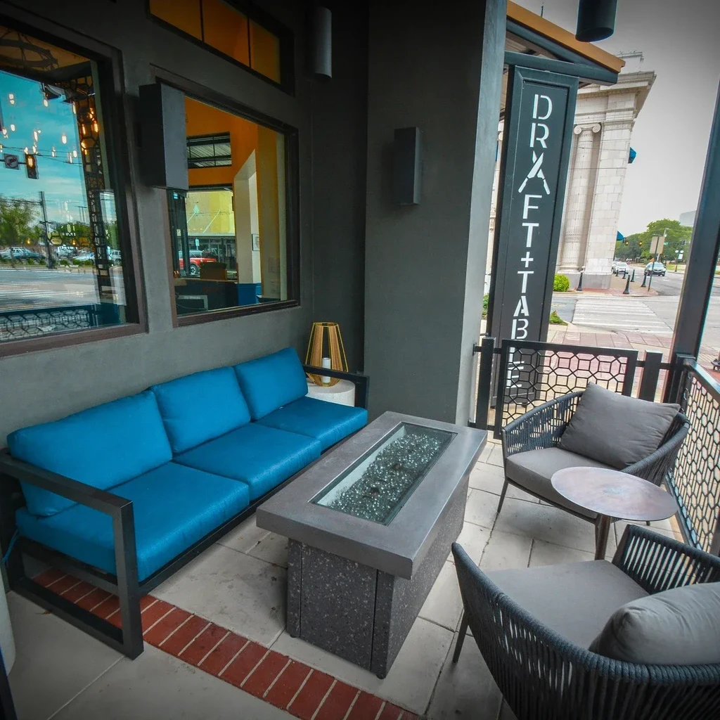 Modern restaurant patio featuring blue sofa, fire pit, and city view.