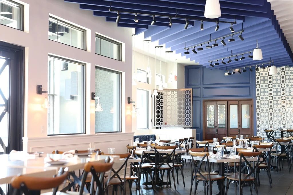 Empty modern restaurant interior: set tables, blue ceiling, geometric wall.