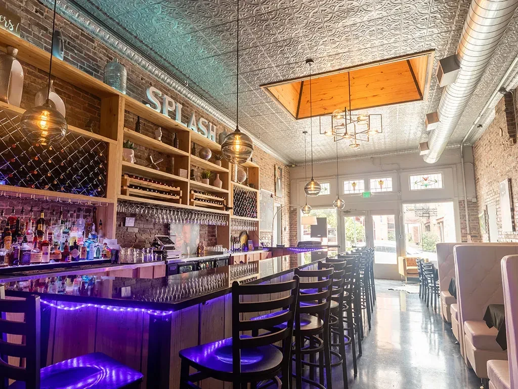 Modern restaurant interior with purple-lit bar, exposed brick, and 'SPLASH' sign.