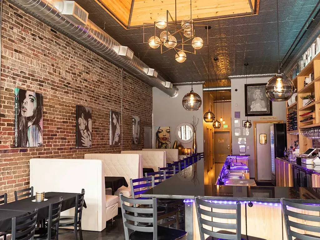Modern restaurant bar interior: brick wall, art, purple-lit bar.