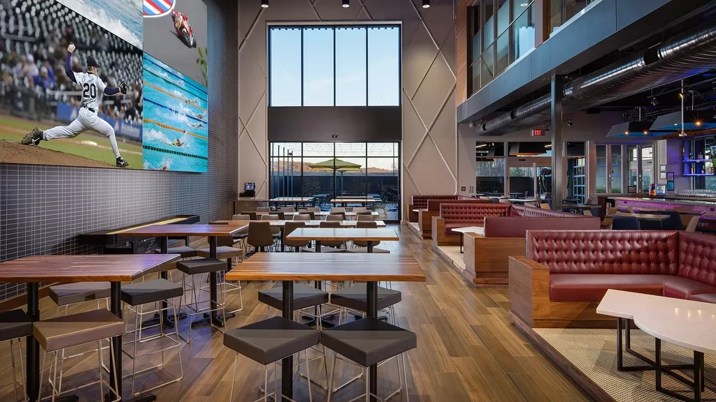 Modern restaurant with huge sports screen, red booths, and purple-lit bar.