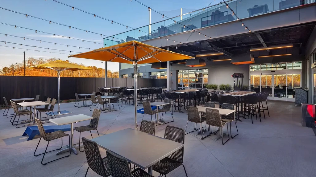 Modern outdoor patio with seating, orange umbrellas, and bistro lights.