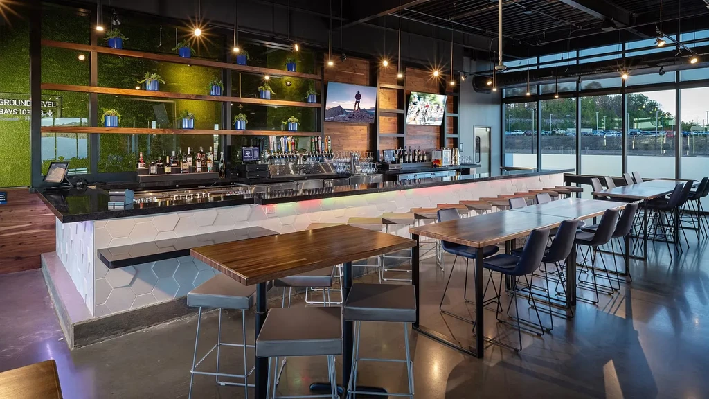 Modern restaurant interior with sleek bar, various seating, and large windows.