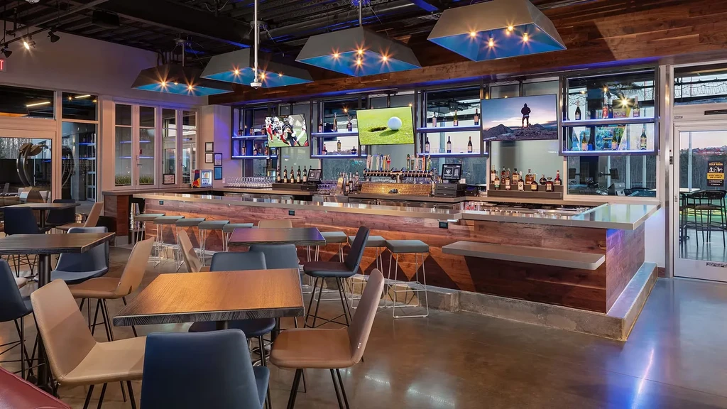 Modern bar and restaurant interior with a long counter and golf course view.