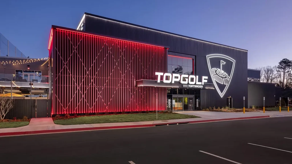 Exterior of modern Topgolf at dusk, with red lights and signage.