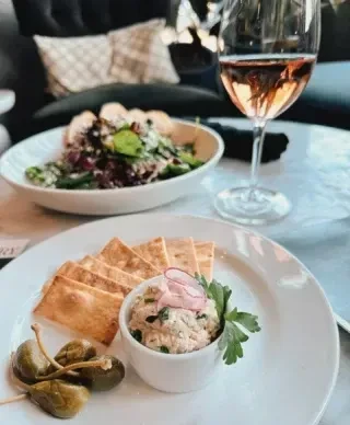 Restaurant table with dip, flatbread, capers, green salad, and rosé wine.
