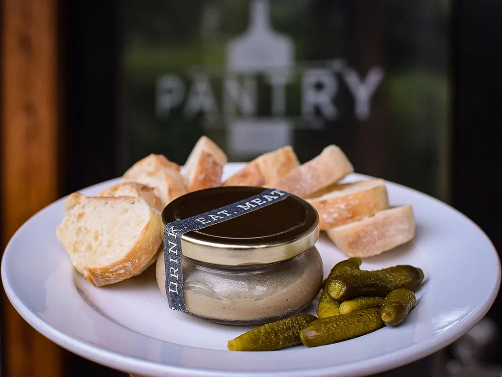 White plate with 'EAT. MEAT.' jar, bread, and gherkin pickles.