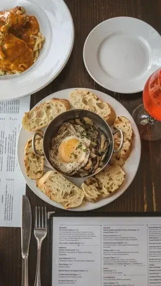 Rustic table with pasta, mushrooms, sunny-side egg, baguette, cocktail, menus.