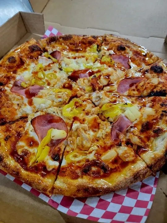 Baked pizza in box with ham, pineapple, chicken, peppers, and BBQ sauce.