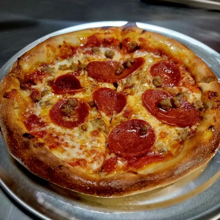 Golden baked pizza with mozzarella, pepperoni, and sausage on a silver pan.