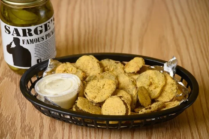 Golden-brown fried pickle chips with sauce, and a jar of pickles.