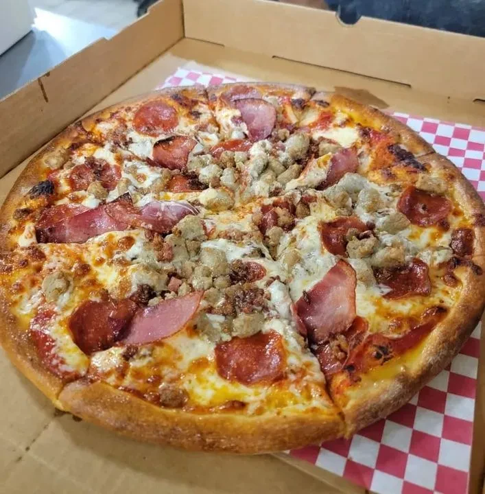 Whole meat-topped pizza with bubbly cheese in a cardboard box.