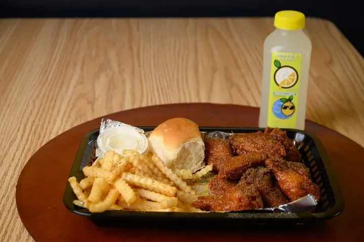 Deep-fried chicken, fries, roll, sauce, and lemonade on a black tray.