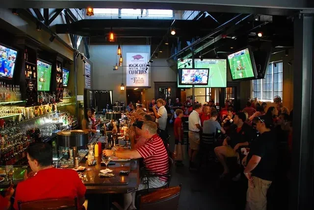 Bustling sports bar interior with patrons, TVs, and a stocked bar.