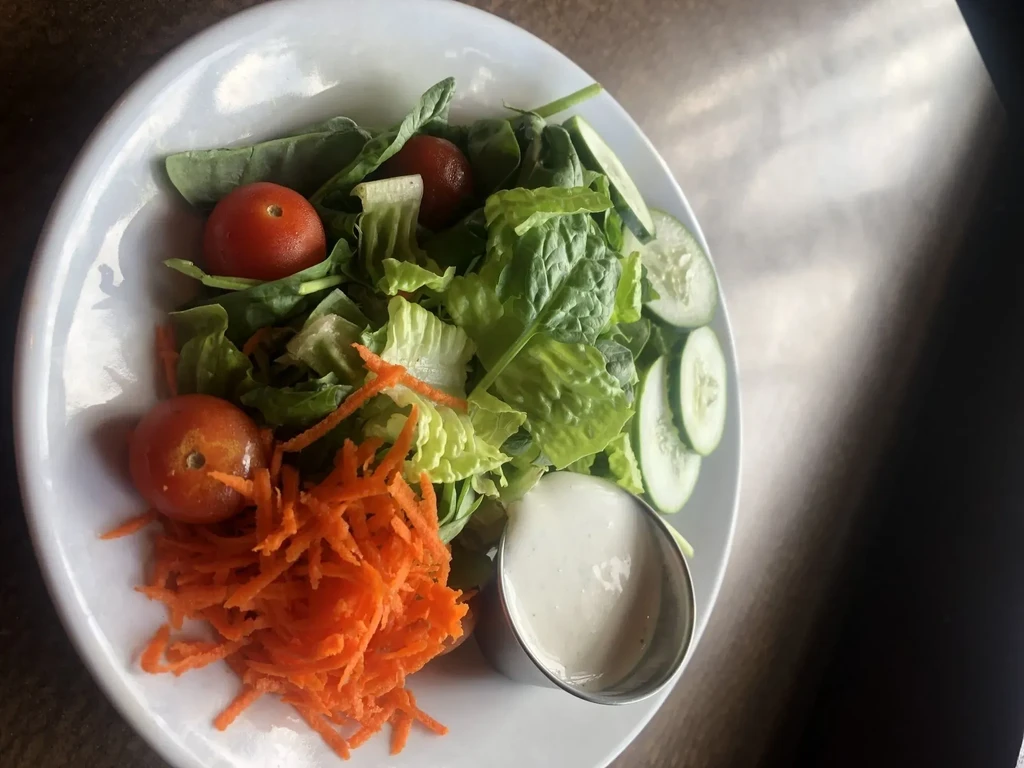 Fresh green salad with tomatoes, shredded carrots, cucumber, dressing.