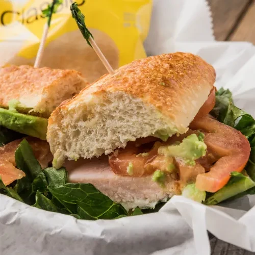 Halved sub sandwich with turkey, lettuce, tomato, avocado in a basket.