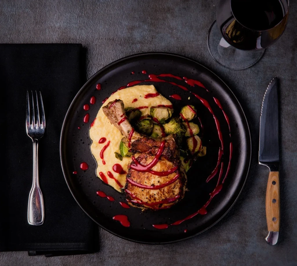 Top-down view of plated pork chop, mashed potatoes, Brussels sprouts, red sauce.