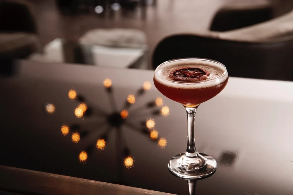 Reddish-brown cocktail with dried citrus and warm bokeh background.