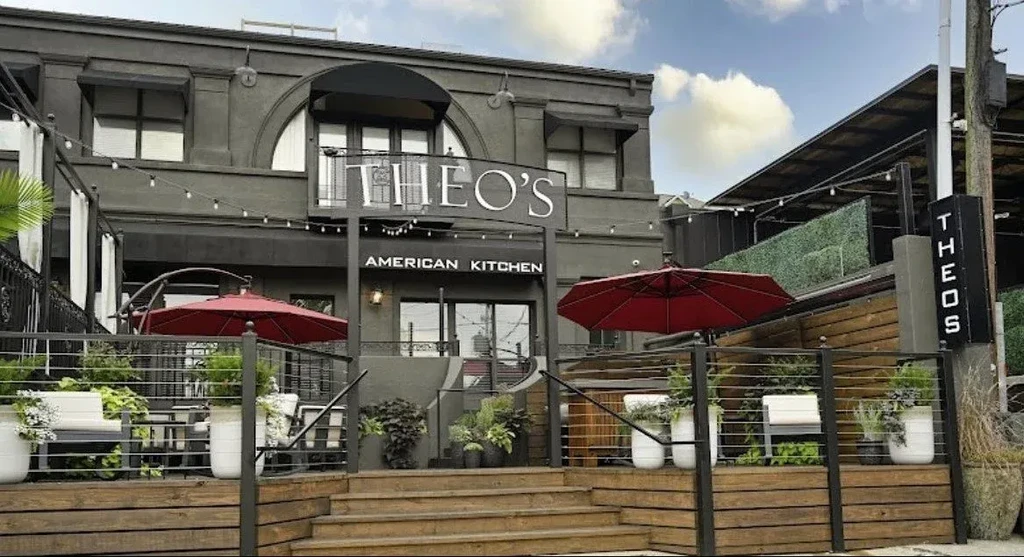 Theo's American Kitchen exterior: dark grey building, multi-level patio with red umbrellas.