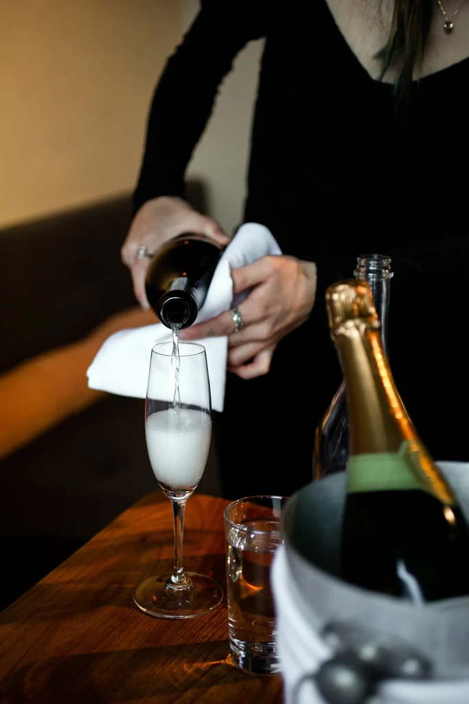 Sparkling wine poured into a flute glass at a dim restaurant.