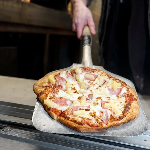 Freshly baked Hawaiian pizza with ham and pineapple on a peel.