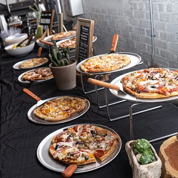 Buffet display of various pizzas, salads, plants, and a brick wall.
