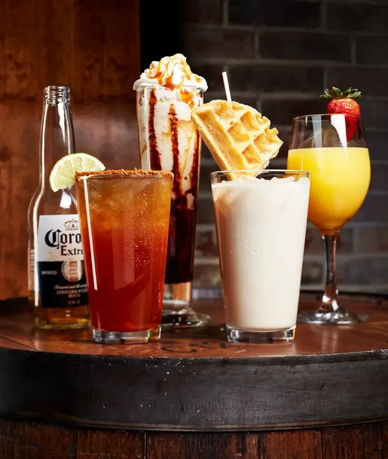 Collection of five garnished drinks and a waffle on rustic wood.