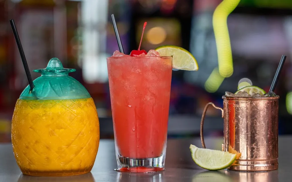 Three colorful drinks: pineapple, red, and copper, on a bar.