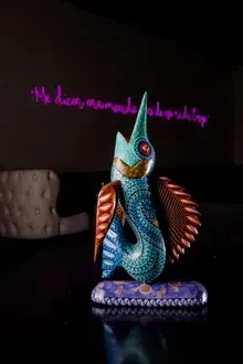 Intricate turquoise fantasy creature sculpture on patterned base, pink neon sign.