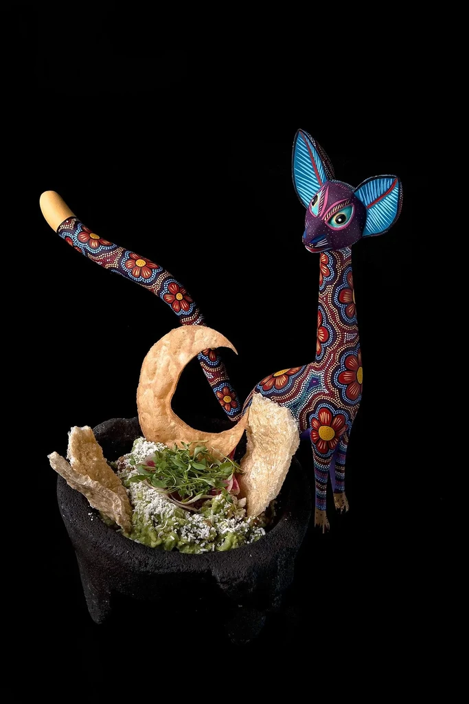 Vibrant guacamole in molcajete with chips, cheese, radish, and alebrije.
