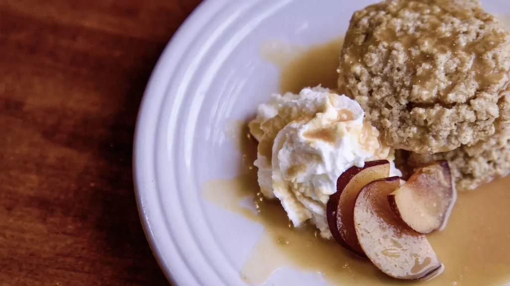 Scone with caramel, whipped cream, and plum slices on a white plate.
