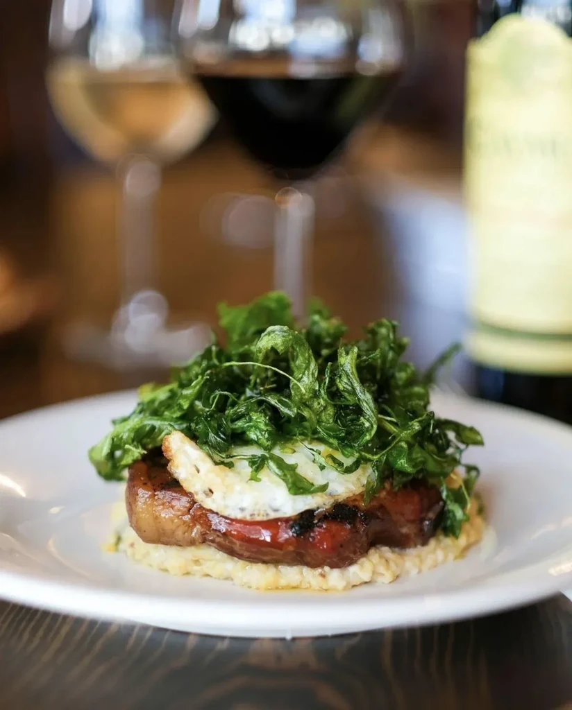 Plated dish with risotto, meat, fried egg, and greens.