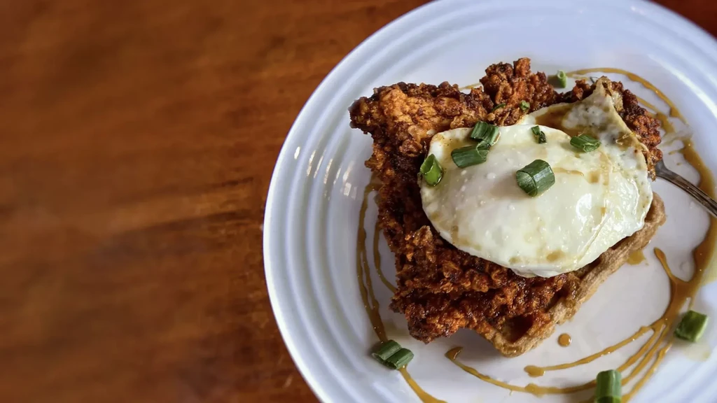 Fried chicken and waffles with a fried egg, green onions, and sauce.