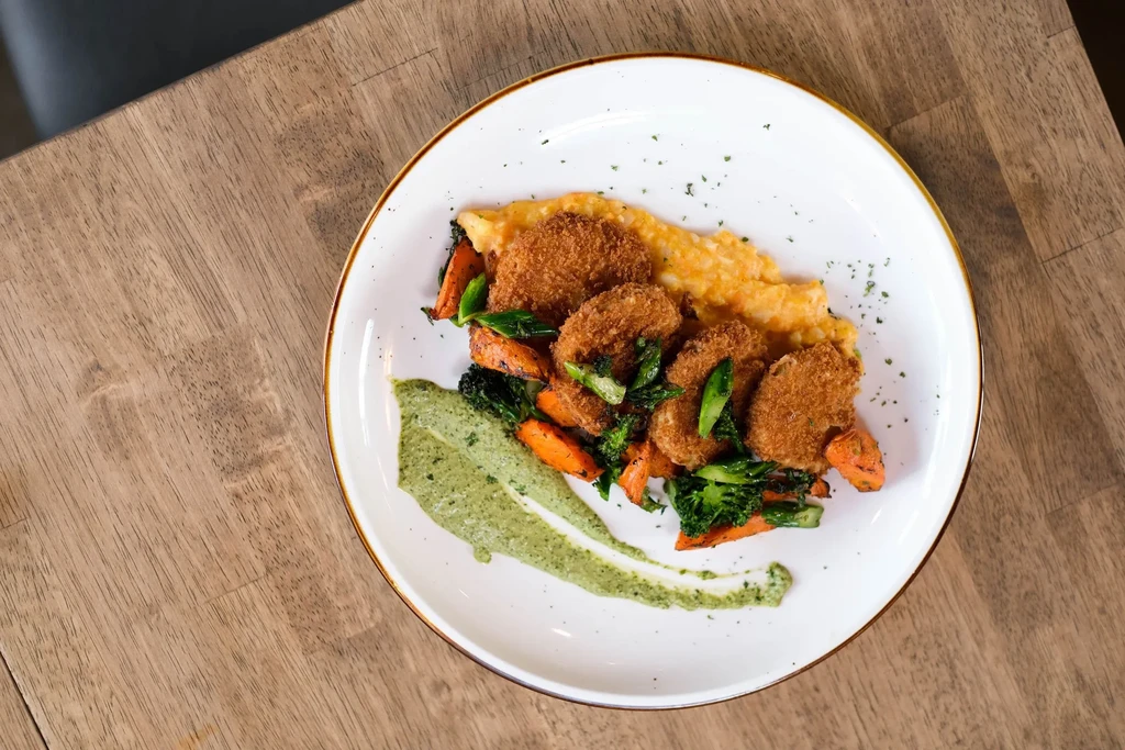 Plated fried seafood, roasted vegetables, mashed potatoes, green sauce.