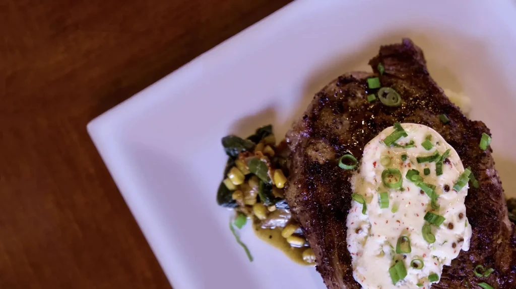 Grilled steak topped with creamy sauce, herbs, and mixed vegetables.
