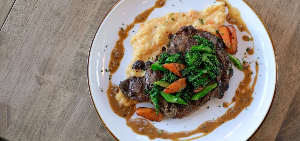 Grilled steak, broccolini, carrots, mashed potatoes, and drizzled brown sauce.