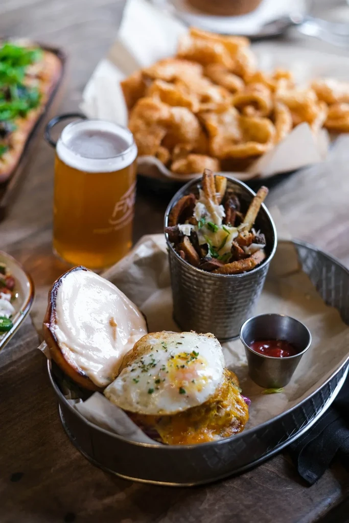 Open-faced burger with fried egg, fries, and a mug of beer.