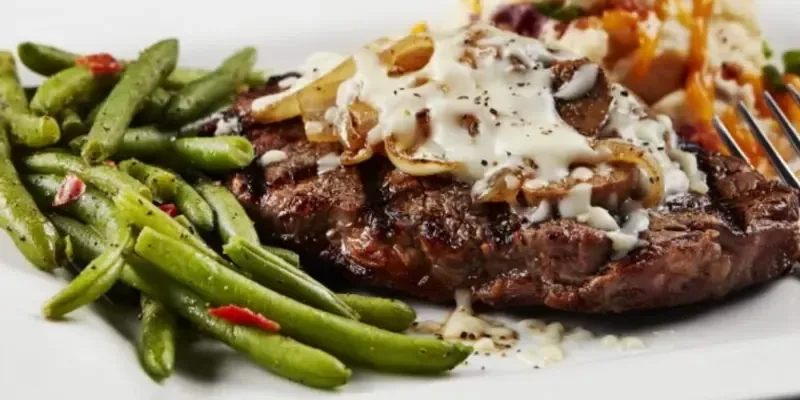 Grilled steak topped with onions, creamy sauce, green beans, mashed potatoes.