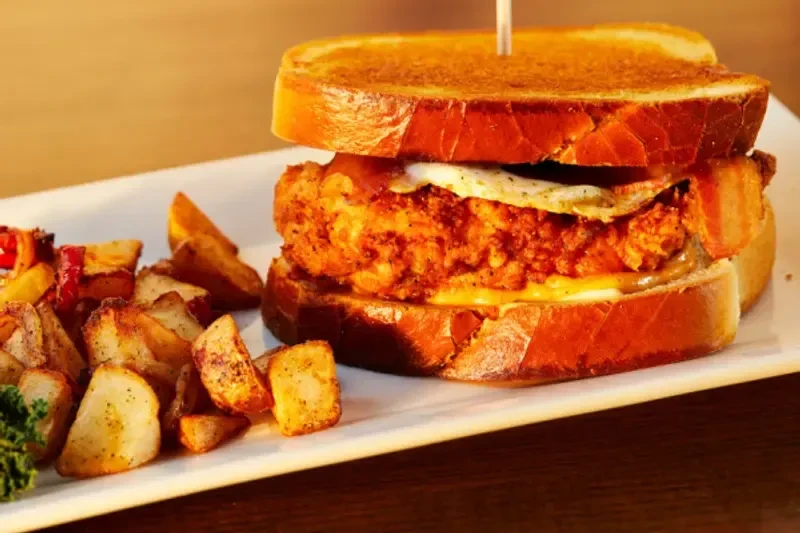 Crispy fried chicken sandwich, fried egg, melted cheese, roasted potatoes, greens.