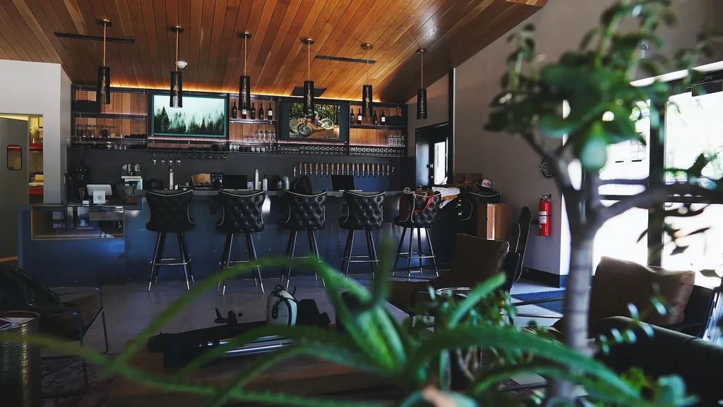 Modern bar interior with dark counter, illuminated bottles, taps, and TVs.