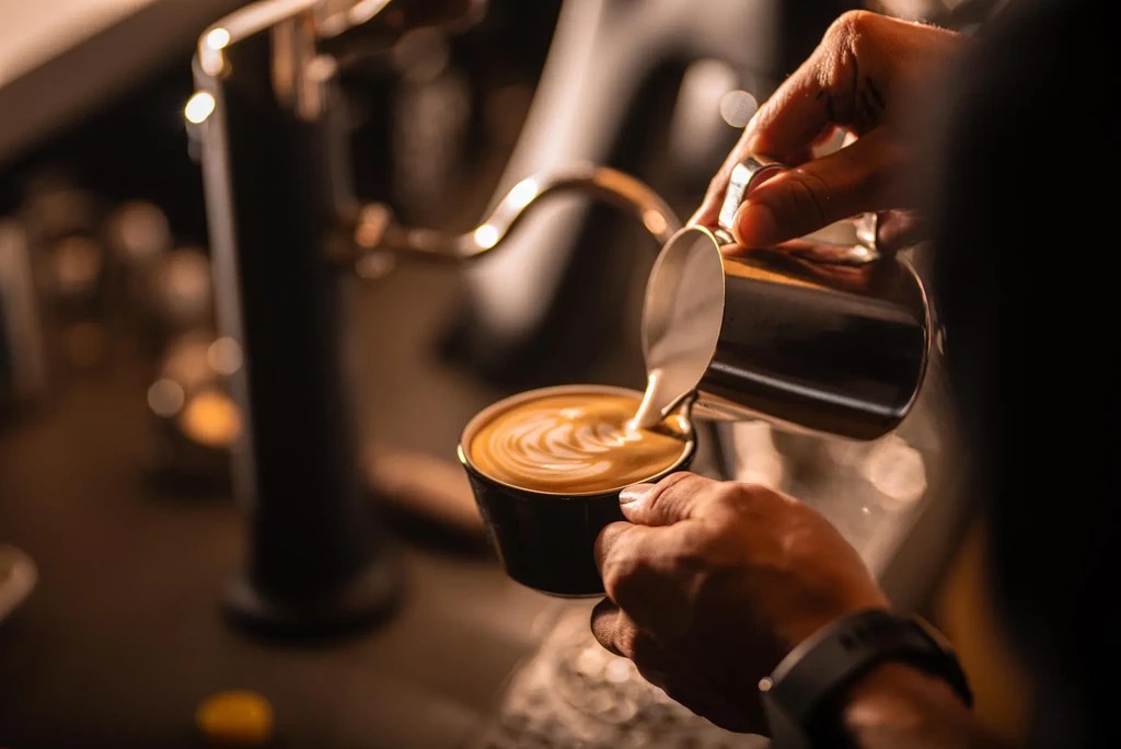 Barista's hands pouring steamed milk into coffee for latte art.