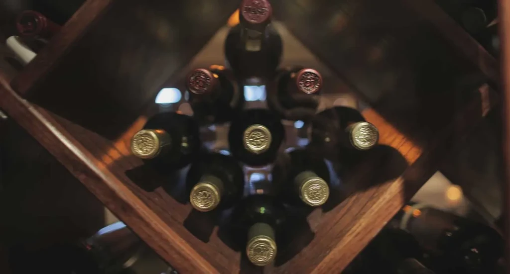 Multiple dark wine bottles in a dark stained criss-cross rack.