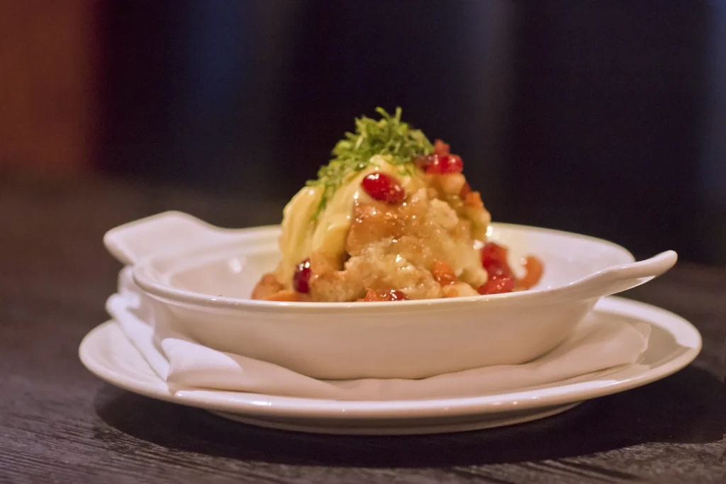 Creamy yellow dish with red berries and green garnish in oval bowl.