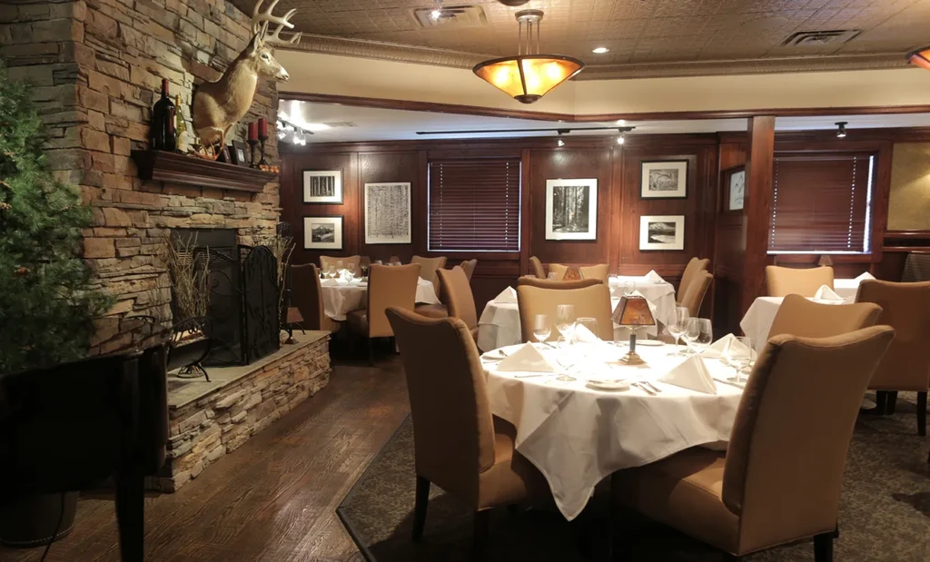 Elegant restaurant dining room with set tables and a stone fireplace.