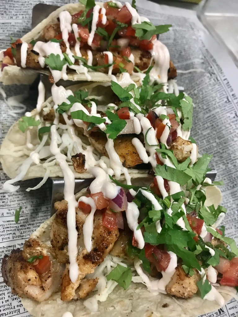 Three generously filled tacos in a metal holder with pico and crema.